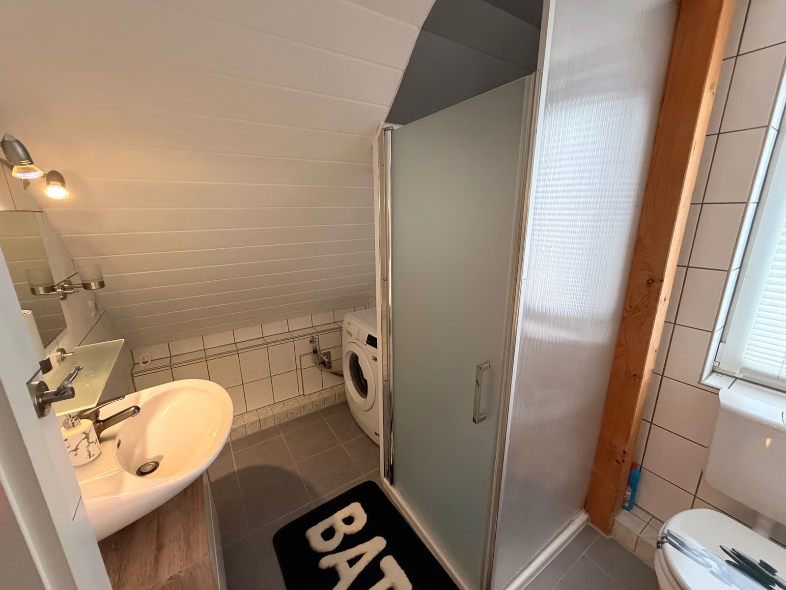 Badezimmer mit Dusche, Waschbecken und Waschmaschine